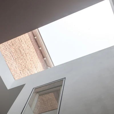 View of a modern interior with a skylight. The ceiling is white, and the skylight frames the sky above, contrasting with the brick building visible through the opening.