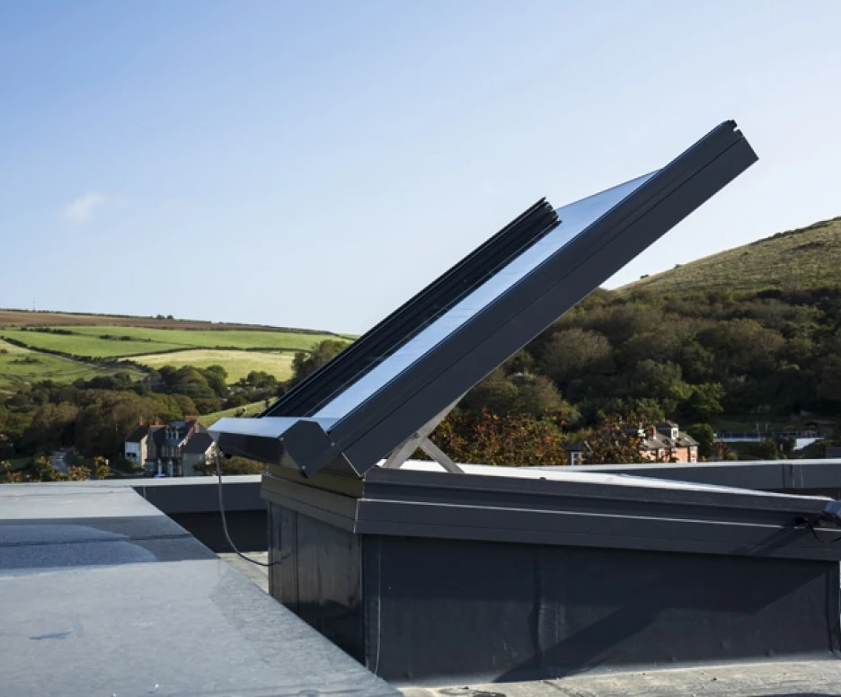 A solar panel system installed on a rooftop, angled to capture sunlight, with a scenic landscape of hills and houses in the background.