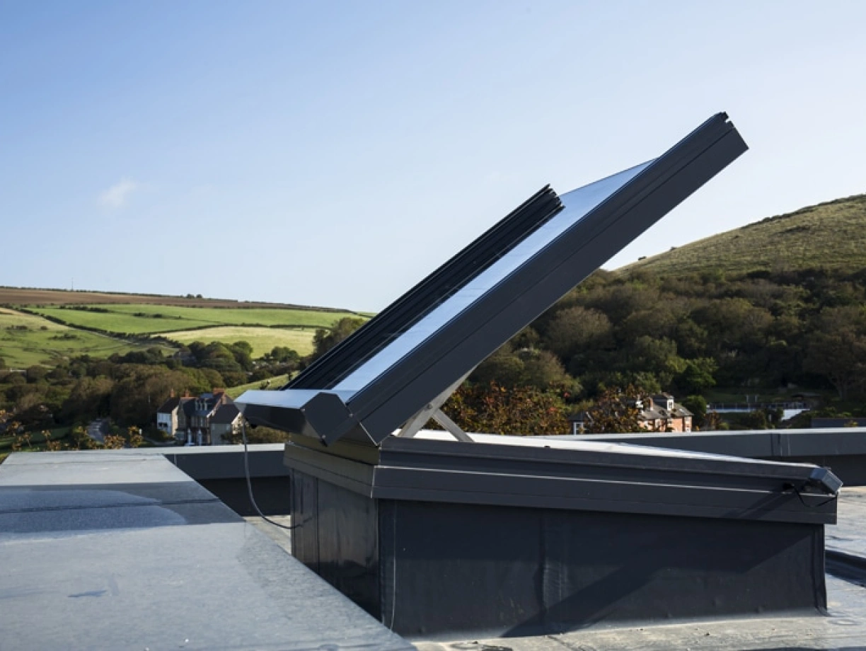 A solar panel system installed on a rooftop, angled to capture sunlight, with a scenic landscape of hills and houses in the background.