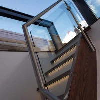 Escalier moderne avec des marches en bois et une rampe en verre et acier inoxydable, sous un plafond vitré laissant entrer la lumière.