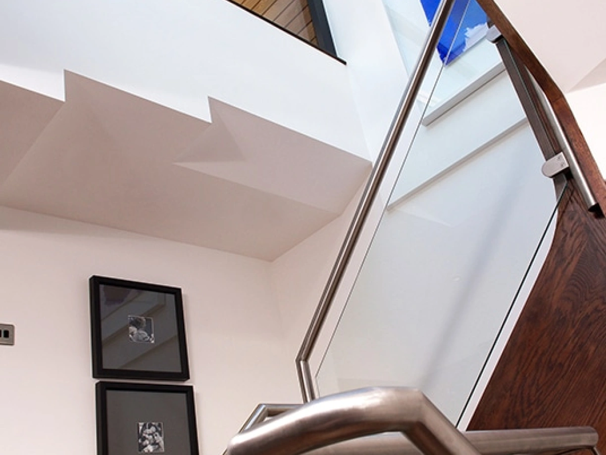 Modern staircase with a sleek metal railing ascending towards a skylight, showcasing a blue painting on the wall. Natural light brightens the interior, highlighting a minimalist design with framed art on the wall.