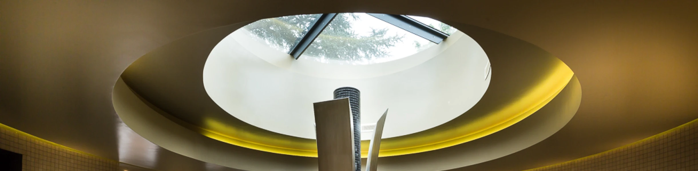 Ein eleganter Spa-Bereich mit einem runden Whirlpool in der Mitte. Über dem Whirlpool befindet sich ein großes, rundes Fenster, das Tageslicht hereinlässt. Die Wände sind gefliest und die Atmosphäre ist entspannend, mit einem modernen Design.