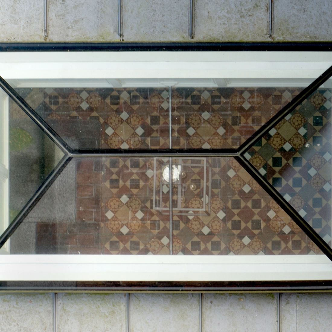 A geometric glass window with a black frame showcases a patterned tiled floor below, reflecting light.