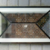 A geometric glass window with a black frame showcases a patterned tiled floor below, reflecting light.