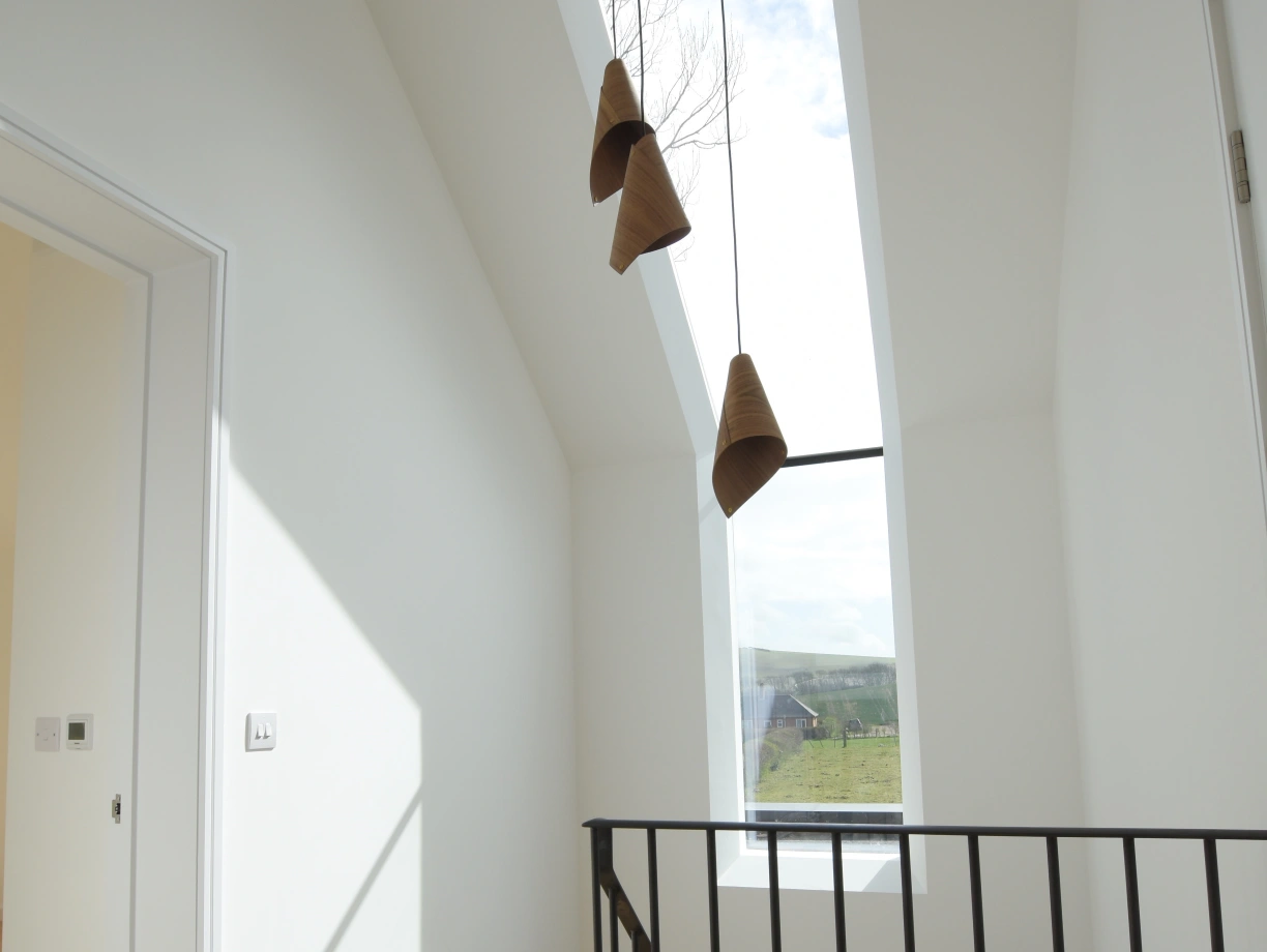Helle Treppe mit Holzfußboden und schwarzem Geländer. Drei hängende Lampen aus Keramik. Großes Fenster lässt Tageslicht herein. Wände und Decken sind weiß gestrichen.