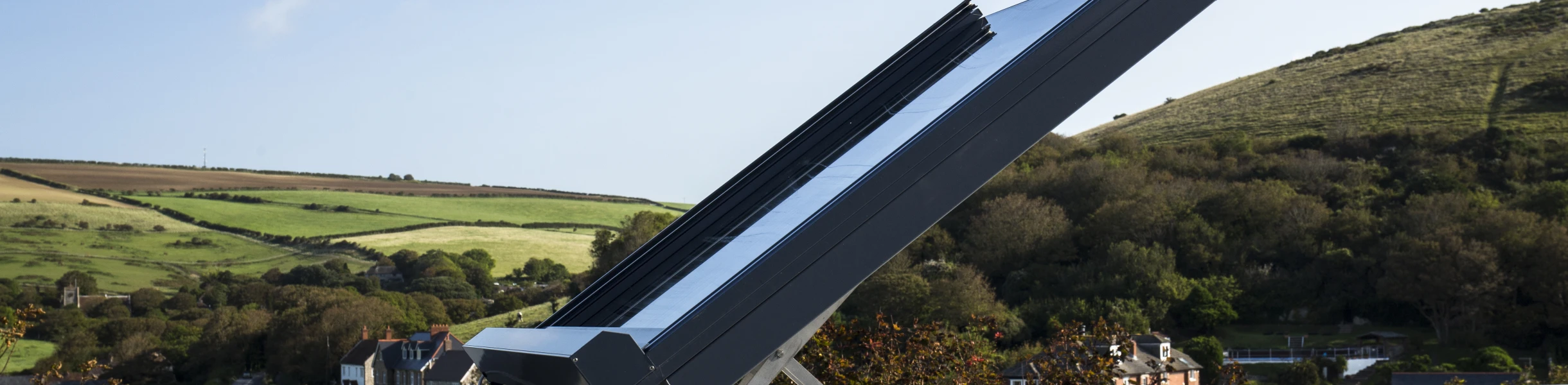 Panneau solaire incliné sur un toit, avec des collines verdoyantes en arrière-plan et un ciel bleu.