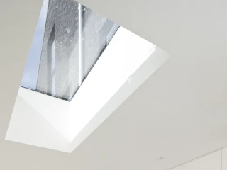 Modern kitchen featuring light-colored wooden cabinetry and a stylish backsplash with geometric patterns in gray, yellow, and pink. A large skylight allows natural light to flood the space, highlighting the minimalist design.
