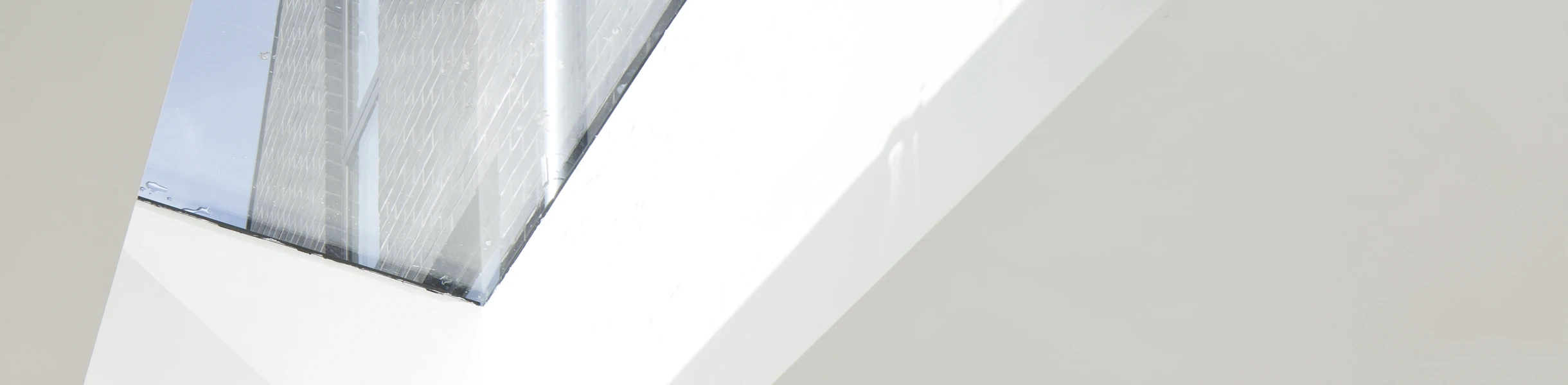 Modern kitchen featuring light-colored wooden cabinetry and a stylish backsplash with geometric patterns in gray, yellow, and pink. A large skylight allows natural light to flood the space, highlighting the minimalist design.