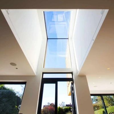 A modern indoor space with large glass windows and a skylight, allowing natural light to flood the room. Outside greenery is visible through the windows, creating a bright and airy atmosphere.