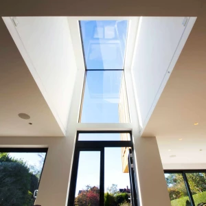 A modern indoor space with large glass windows and a skylight, allowing natural light to flood the room. Outside greenery is visible through the windows, creating a bright and airy atmosphere.