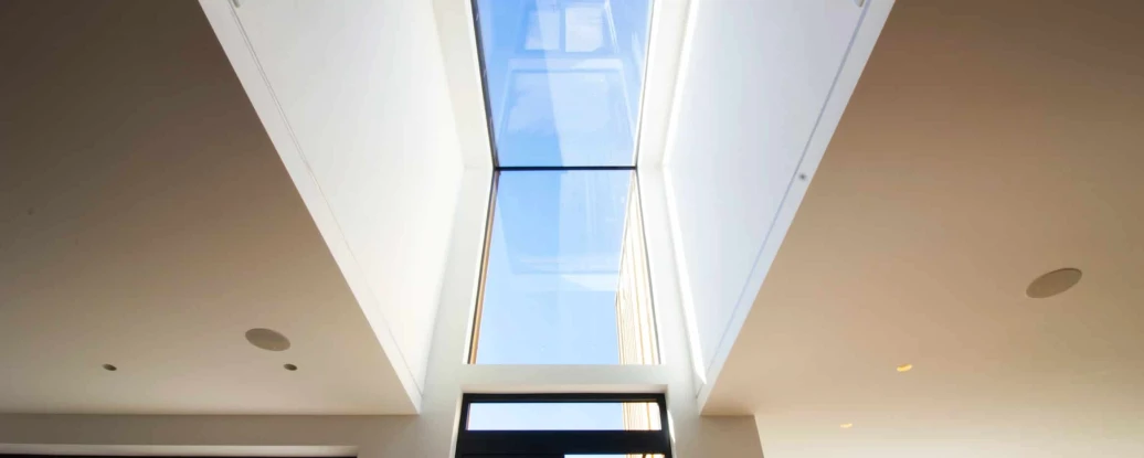 A modern indoor space with large glass windows and a skylight, allowing natural light to flood the room. Outside greenery is visible through the windows, creating a bright and airy atmosphere.