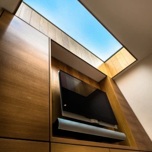 A wooden wall with a tv on it. Above it letting natural daylight in.