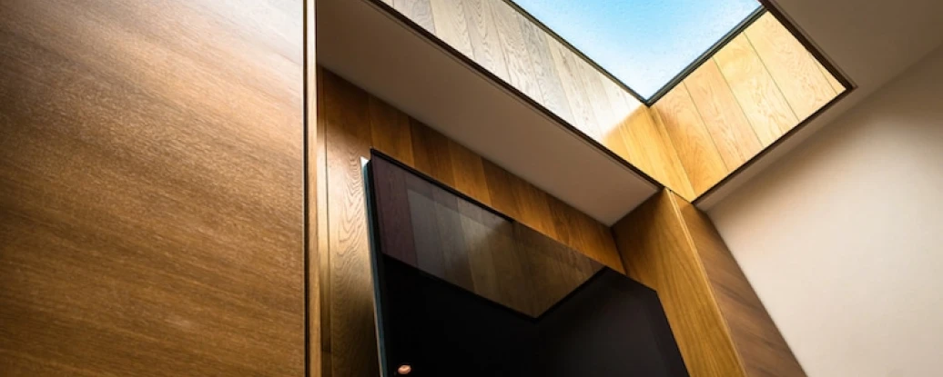 A wooden wall with a tv on it. Above it letting natural daylight in.