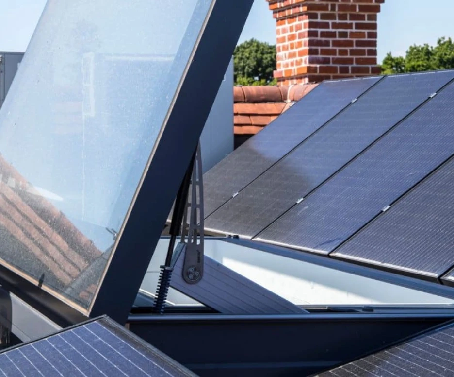 Panneaux solaires installés sur un toit, avec un couvercle en verre relevé dévoilant l’intérieur. Une unité de climatisation est visible en arrière-plan.