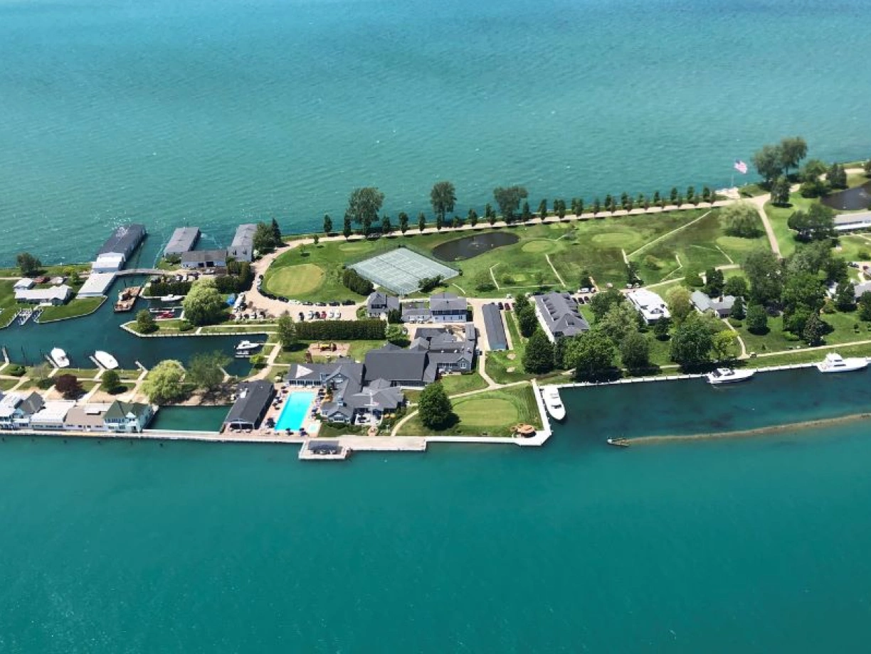 Aerial view of a waterfront property with multiple buildings, green lawns, and boats along a canal. The vibrant blue water contrasts with the lush greenery and well-maintained structures.