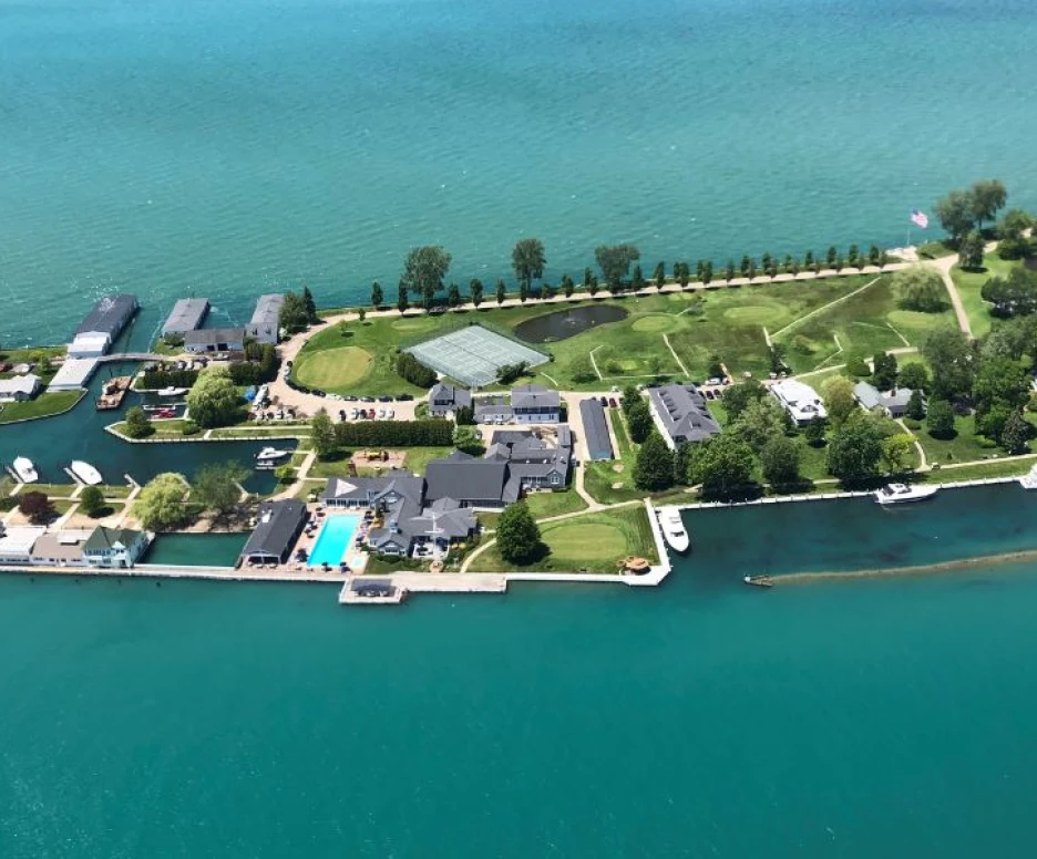 Aerial view of a waterfront property with multiple buildings, green lawns, and boats along a canal. The vibrant blue water contrasts with the lush greenery and well-maintained structures.