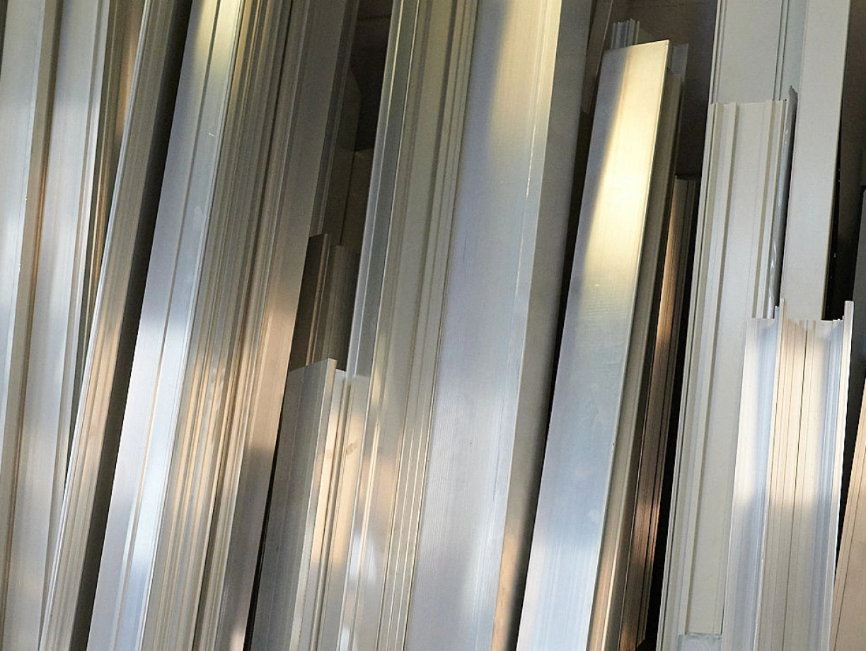 Gestapelte Aluminiumprofile in verschiedenen Größen und Formen, die im Licht glänzen.