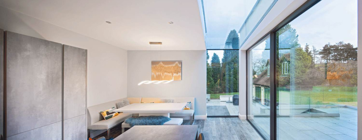 Interior moderno con comedor minimalista y grandes ventanales que ofrecen vista a un jardín. La luz natural ilumina el espacio, que presenta una paleta de colores neutros.