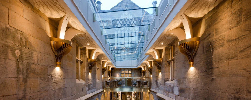 A spacious interior with a staircase leading down to a lively dining area. The walls feature exposed stone, and large windows allow natural light to fill the space. Elegant lighting and modern furnishings complement the historic architecture.