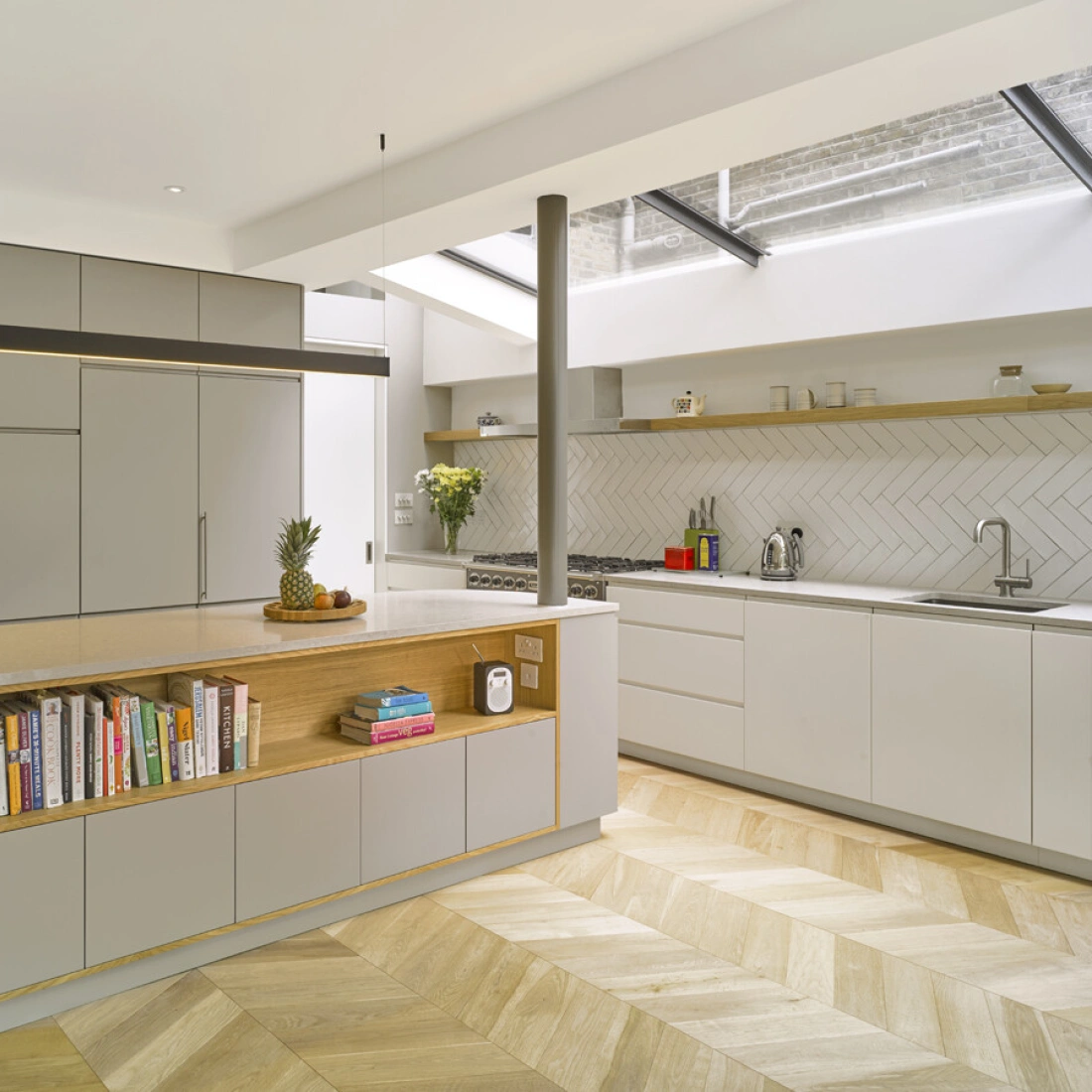 Shows a bright kitchen with grey cabinets with books inside and over looking to the right is multi part skylight