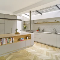 Shows a bright kitchen with grey cabinets with books inside and over looking to the right is multi part skylight