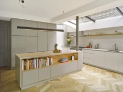 Shows a bright kitchen with grey cabinets with books inside and over looking to the right is multi part skylight