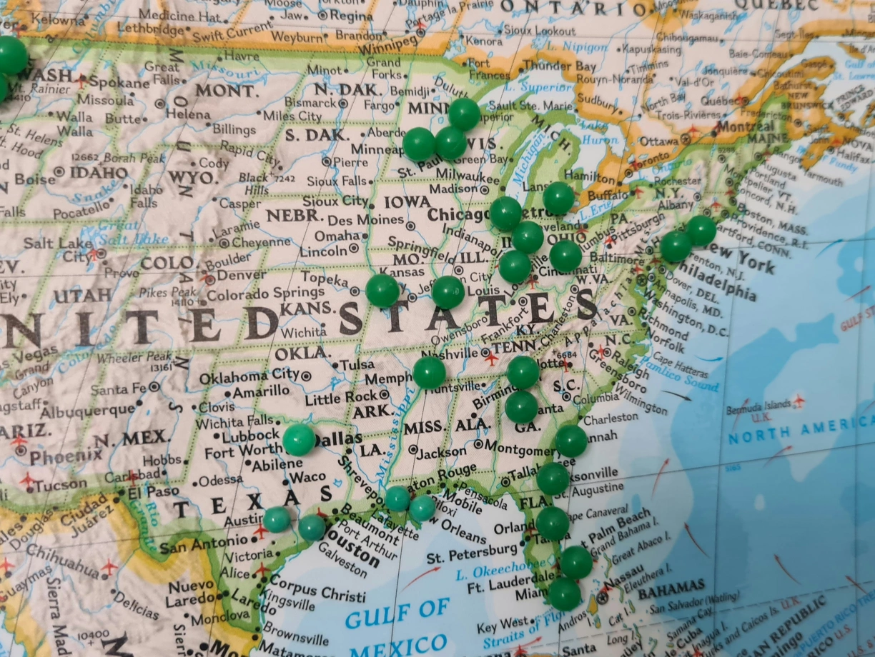 A detailed map of the United States featuring multiple green pushpins marking various locations, including states and cities across the country. The Gulf of Mexico and the Atlantic Ocean are visible along the southern and eastern edges, respectively.