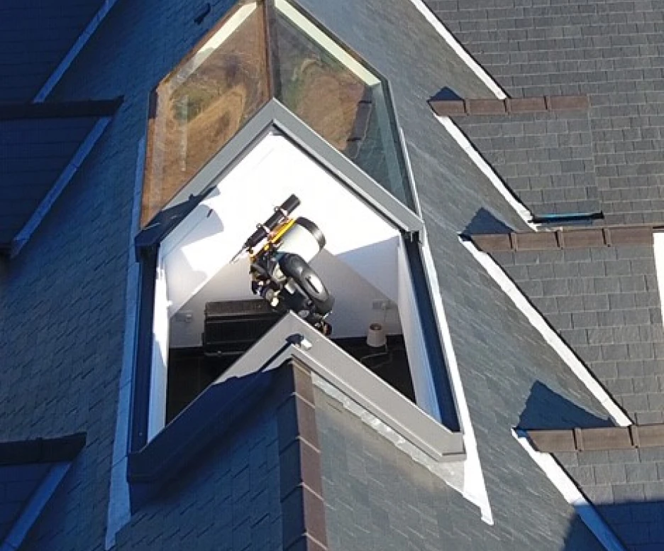 A triangular skylight on a roof, revealing a small space with a vacuum cleaner and some household items inside.