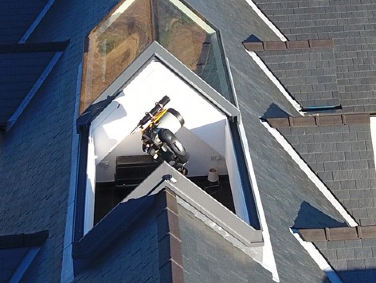 Ventana en el techo de una casa con forma triangular, que muestra el interior. Hay un tambor y un objeto negro en el espacio iluminado.