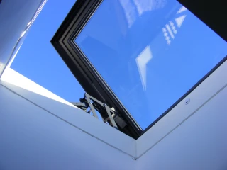 A skylight with a modern frame, showing a clear blue sky above. The interior walls are white and angular, creating a bright and open atmosphere.