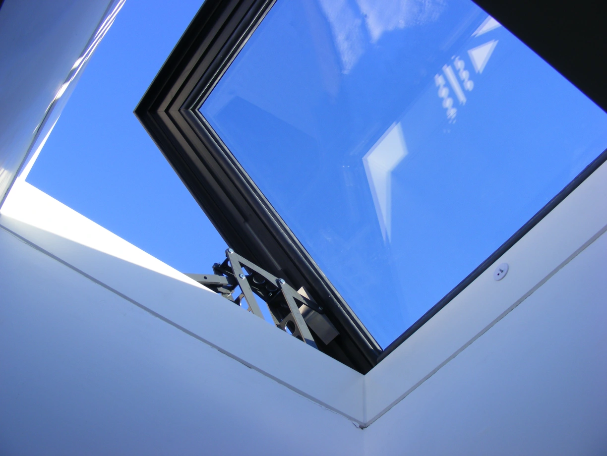 A skylight with a modern frame, showing a clear blue sky above. The interior walls are white and angular, creating a bright and open atmosphere.