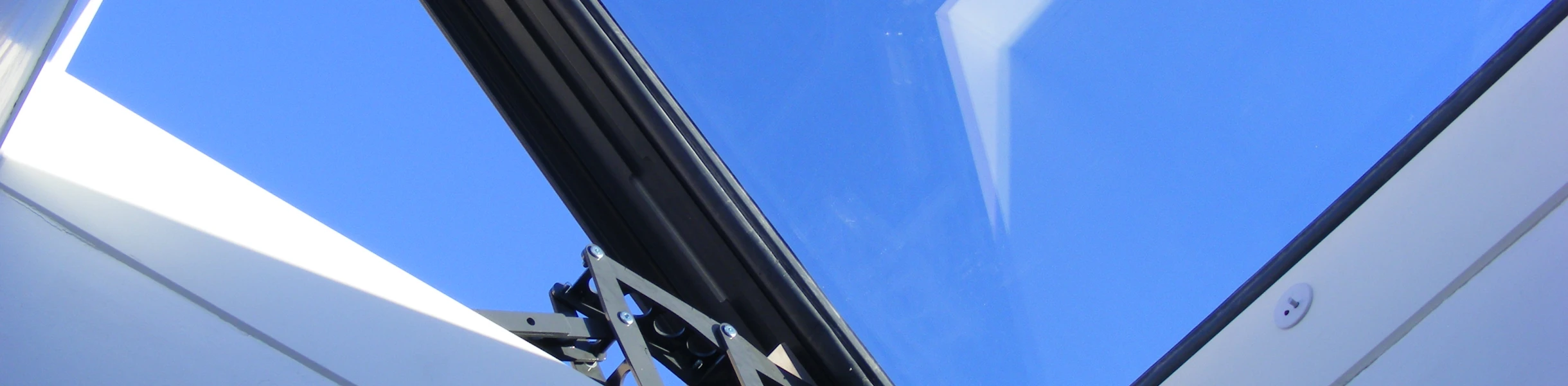 A skylight with a modern frame, showing a clear blue sky above. The interior walls are white and angular, creating a bright and open atmosphere.