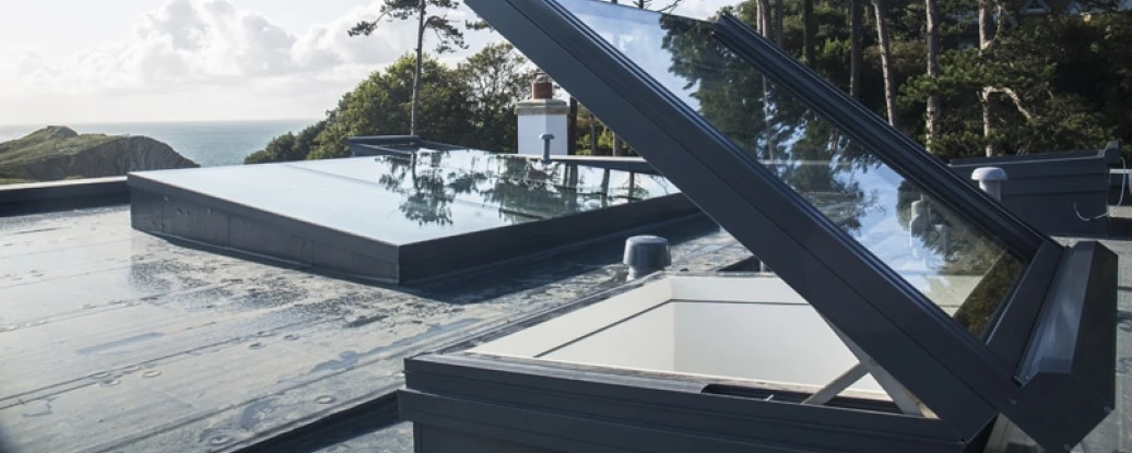 Sky lights on a flat roof with ocean views and trees in the background. Bright blue sky with a few clouds.