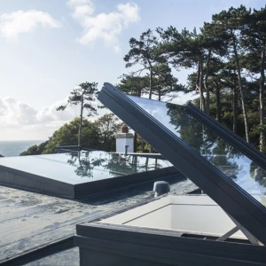 Sky lights on a flat roof with ocean views and trees in the background. Bright blue sky with a few clouds.