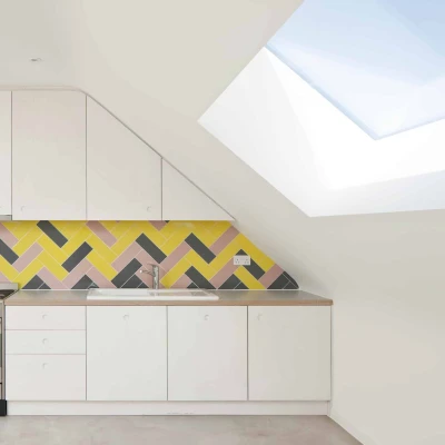 Modern kitchen featuring white cabinets and a colorful herringbone-patterned backsplash in yellow, pink, and gray. A stainless steel stove sits against the wall beneath a skylight that adds natural light to the space.