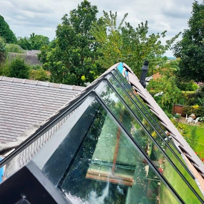 A sloped roof with large glass panels reflects greenery and a garden below, showcasing a cloudy sky in the background.