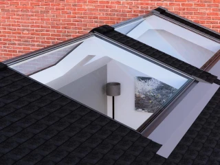 Tres tragaluces en un tejado negro, con una pared de ladrillos rojos al fondo. Se puede ver una lámpara y una obra de arte a través de los tragaluces.