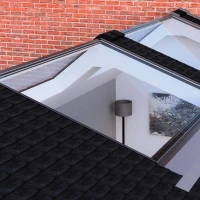 Two skylights on a sloped roof provide a view into a brightly lit interior space featuring a gray lamp and a piece of art on the wall. The roof is covered in dark shingles, and a brick wall is visible in the background.