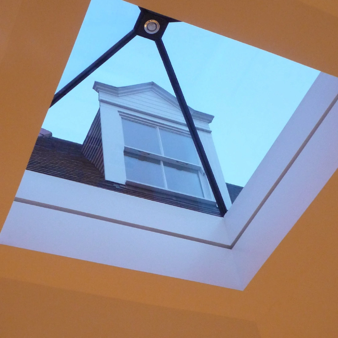 Fenestre de tet, montrant un ciel clair e un pavillon arquitectonic. Elemente metallic forme un triam de supporto.