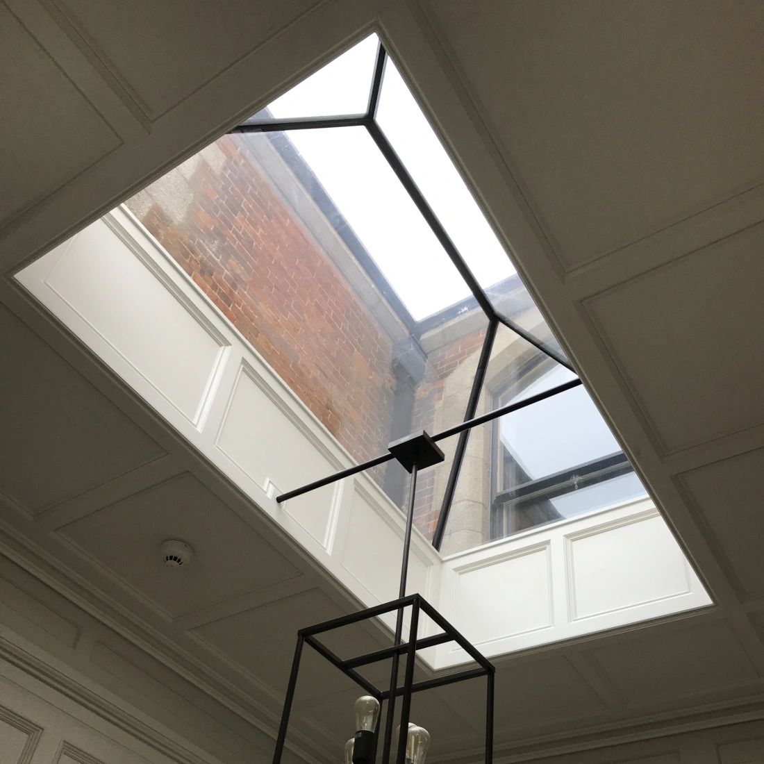 Plafond en panneaux avec un puits de lumière et un lustre noir moderne. La lumière naturelle éclaire l'espace intérieur.