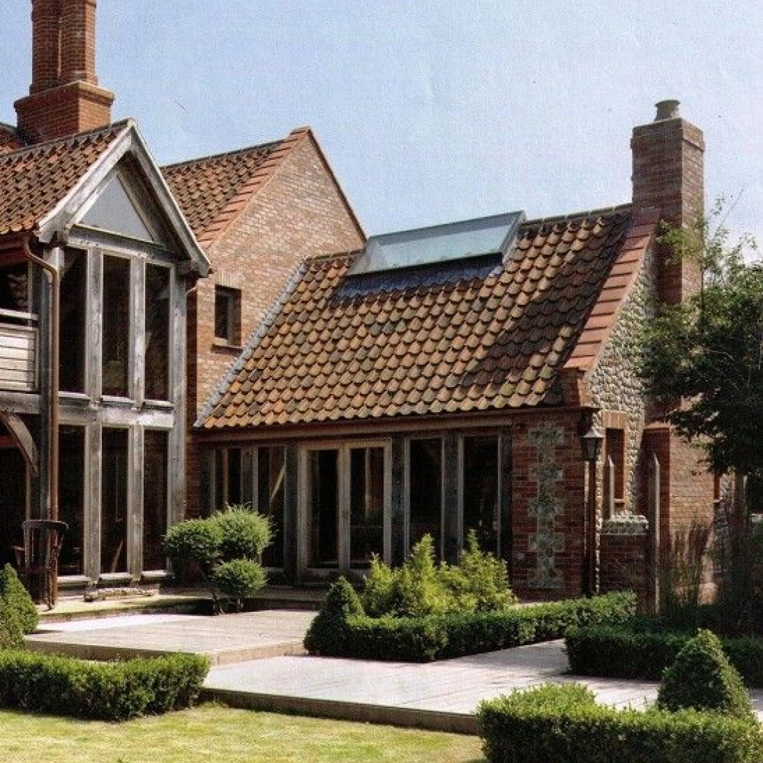 Haus con arquitectura moderna e tradizional, presenta paretes de vetro e teulada de tegole. Jardin ben curat con boscheti verde.