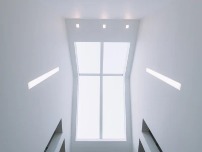 Blick nach oben in einen modern gestalteten Raum mit weißen Wänden und dreieckigen Fenstern, die Tageslicht hereinlassen. An der Decke befinden sich mehrere gleichmäßig verteilte Lichtquellen.