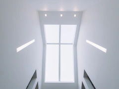 Techo interior con una ventana grande que deja pasar luz natural. Paredes blancas y luces empotradas. Escalera visible en la parte inferior.