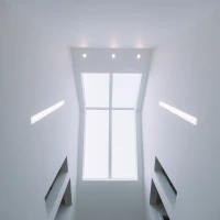 A view looking up at a bright skylight surrounded by minimalist white walls, with recessed lights illuminating the space.