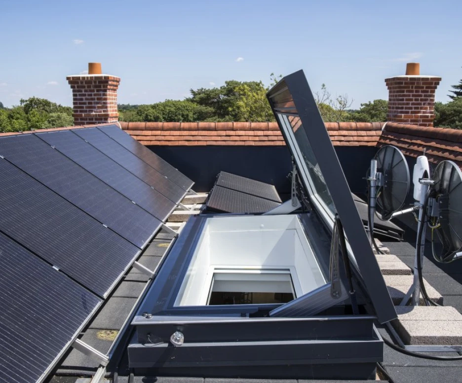A rooftop featuring solar panels, with a skylight opening and satellite dishes installed nearby. The setting is sunny, with trees visible in the background.