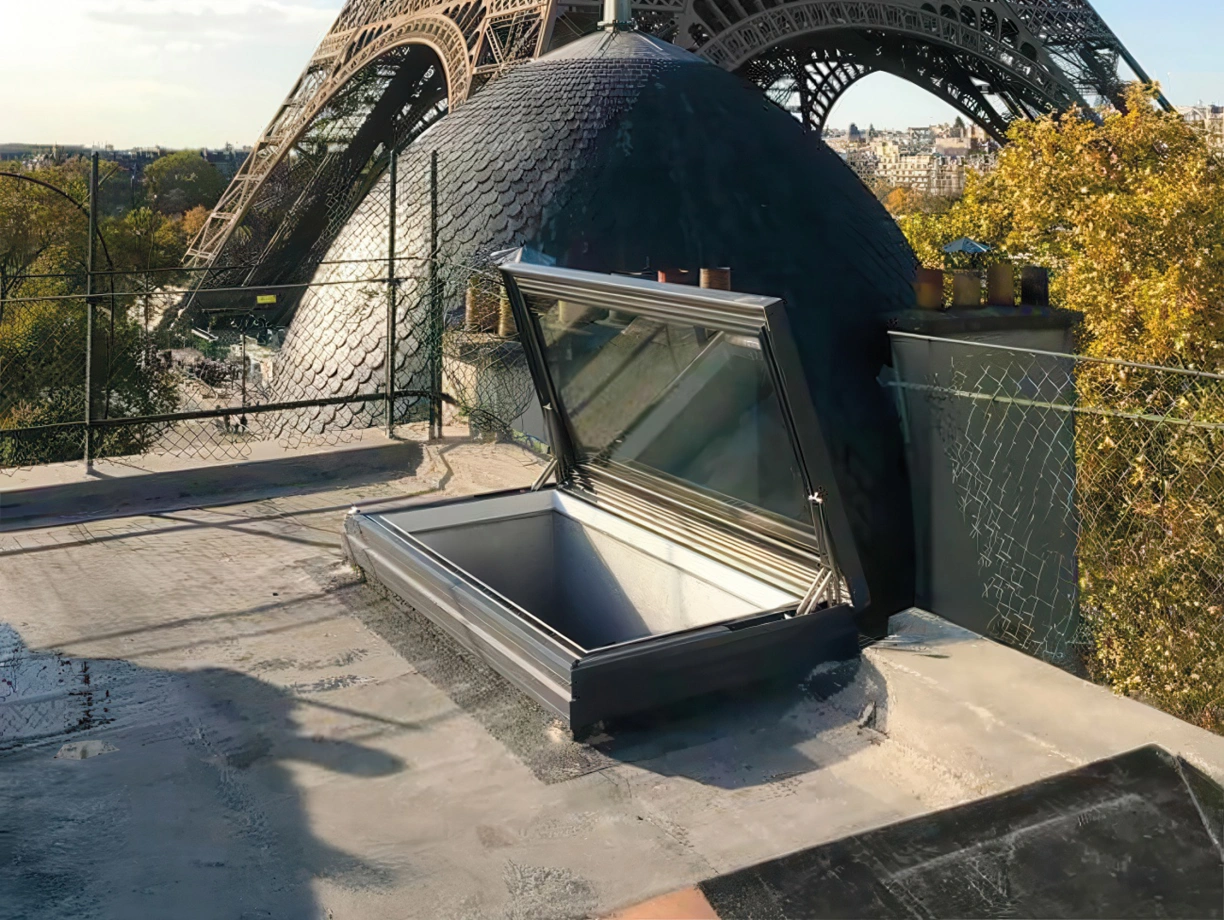 A rooftop view featuring the Eiffel Tower in the background, with a large dome and an open skylight in the foreground. Clear blue sky and autumn foliage are visible.