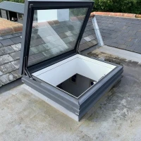 Un lucerna opening sur un tegment gris, con muros interior blanc. L'area circumjacent es de concreto. In distantia, vegetazione verd e edifices.