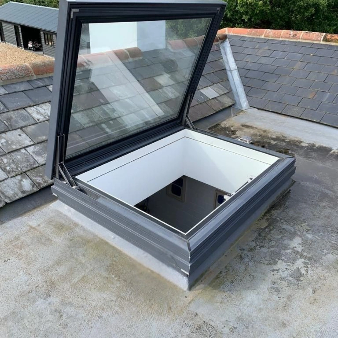 Un lucerna opening sur un tegment gris, con muros interior blanc. L'area circumjacent es de concreto. In distantia, vegetazione verd e edifices.