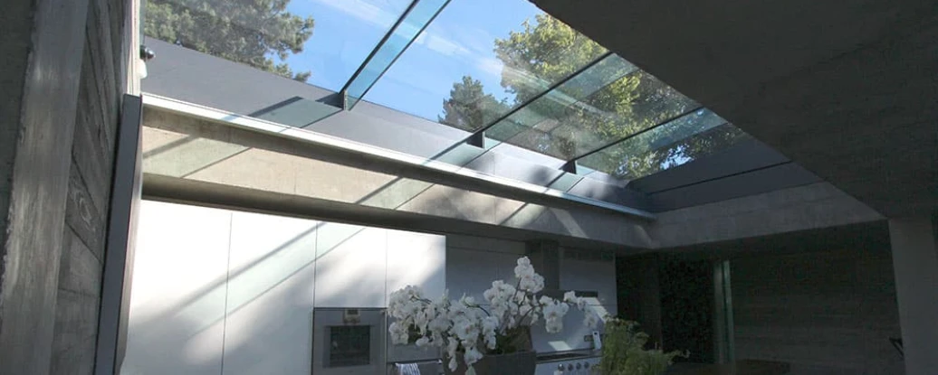 A modern kitchen featuring a sleek design with white cabinetry, a dark countertop, and large glass skylights that allow natural light to flood the space. An arrangement of white orchids adds a decorative touch.