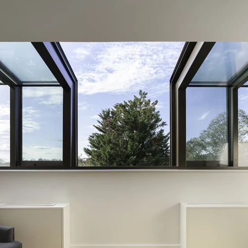 Ein moderner Raum mit großen, geöffneten Fenstern, die eine Aussicht auf einen grünen Baum und einen klaren Himmel bieten. Der Boden ist aus hellem Holz und zwei weiße Heizkörper stehen an der Wand.